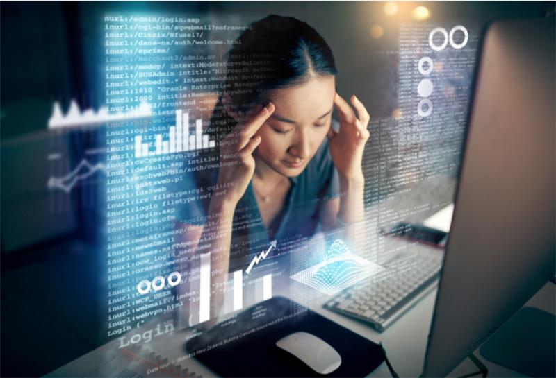 Woman holding her head in frustration while working on a computer surrounded by digital data graphics